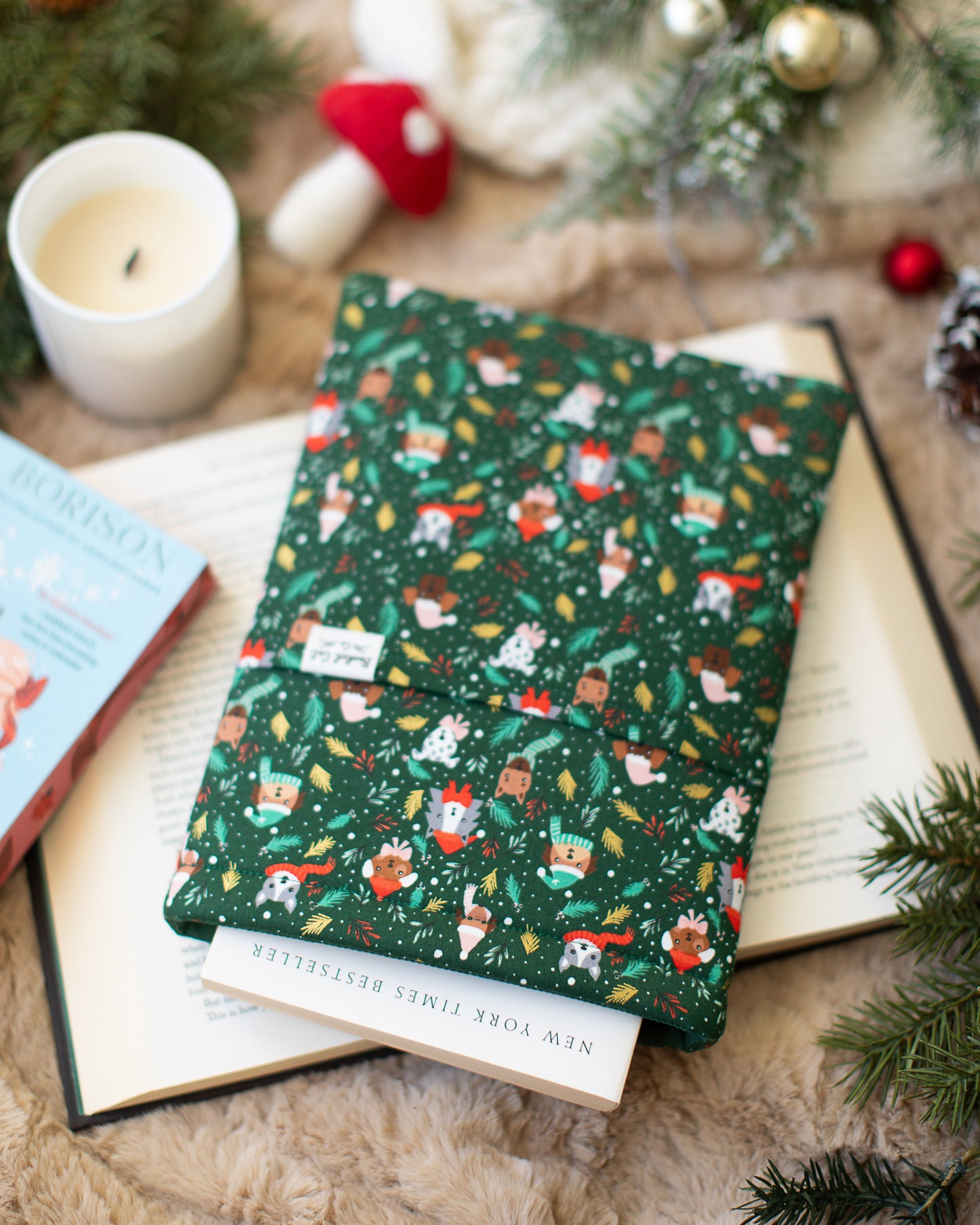 A green book sleeve with dogs on top of an open book, surrounded by Christmas decorations.