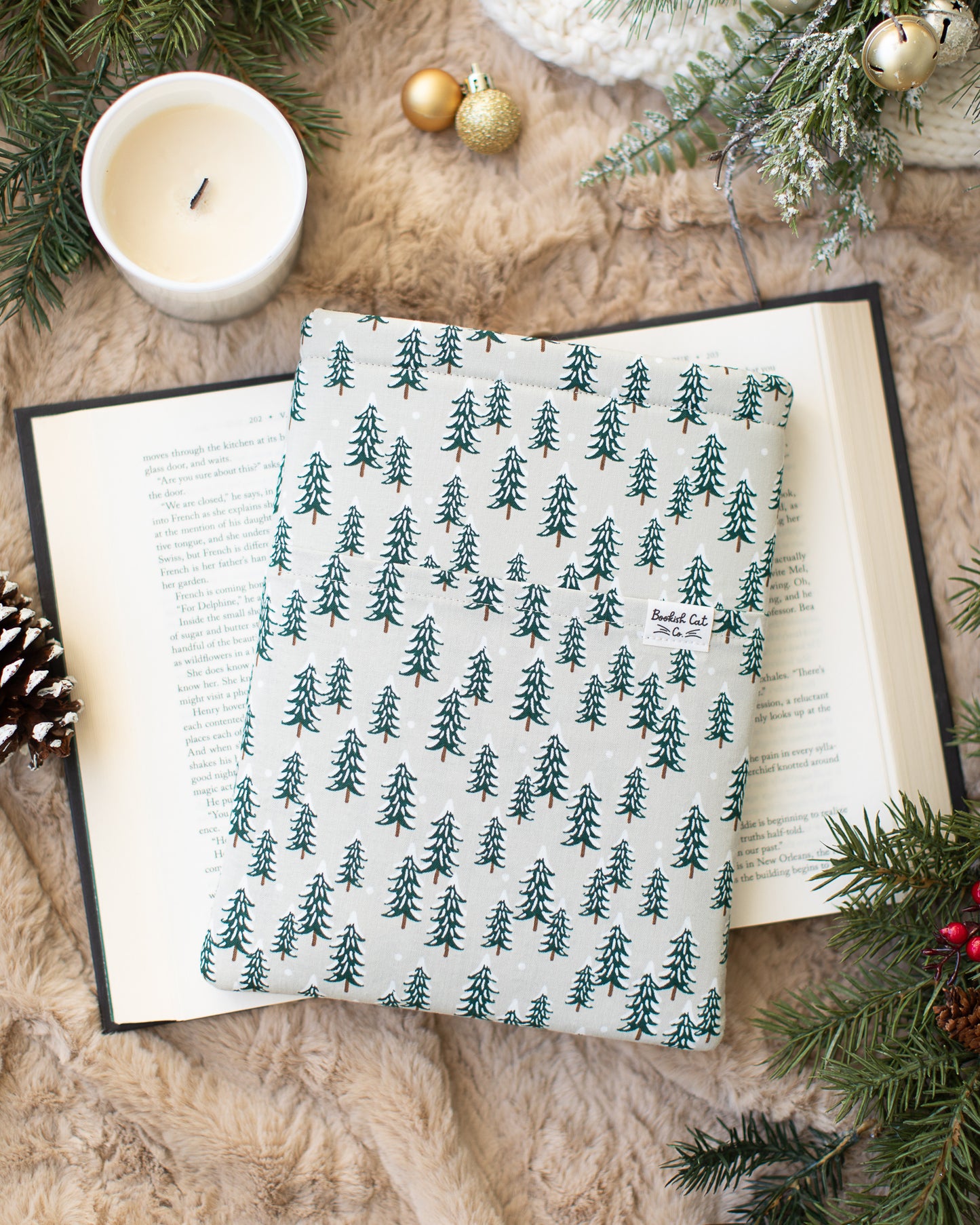 Christmas trees with snow book sleeve, made with Rifle Paper Co fabric. Neutral beige background with evergreen trees.